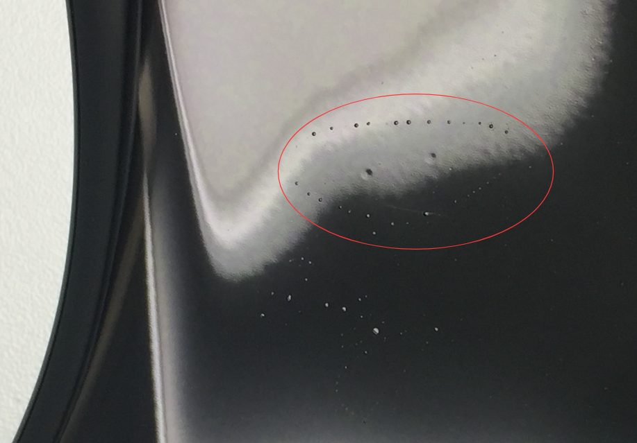 Glossy black printed surface with a cluster of small circular craters (fisheyes), circled in red