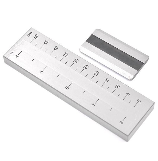 A Hegman grind gauge — a steel block with a tapered groove marked in microns and Hegman units — with its scraper