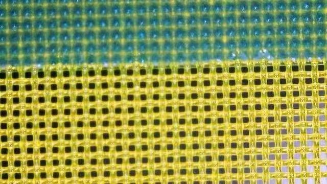 A polyester screen under a magnifier: the upper green area is sealed with emulsion, the lower yellow area is open mesh